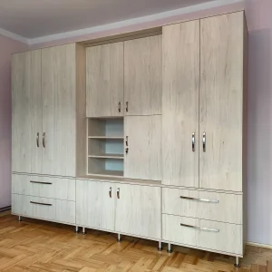Duża szafa i komoda na wymiar w jasnym dekorze drewnopodobnym z licznymi szufladami i półkami w pokoju mieszkalnym.